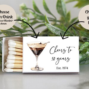 Puede incluir: Caja de cerillas blanca con una ilustraci&oacute;n en blanco y negro de un espresso martini. El texto en la caja de cerillas dice "Cheers to 50 years Est. 1974".