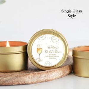May include: Gold candle tin with a white label that says "Whitney's Bridal Shower" with a champagne glass graphic. The label also includes the text "Thanks for celebrating with us! 08.14.20xx."