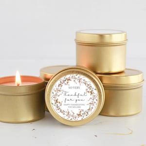May include: Four gold candle tins with a white label that says "So Very Thankful for you Happy Thanksgiving The Millers". The label has a floral design with brown and orange flowers.