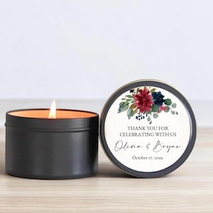 May include: A lit black candle in a round tin next to a tin with a floral design and text that reads "Thank you for celebrating with us" and the names Olivia & Bryan, and the date October 17, 20xx.