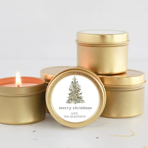 May include: Four gold candle tins with a white label. The label has a drawing of a Christmas tree and the text "merry christmas love, the mckinneys".