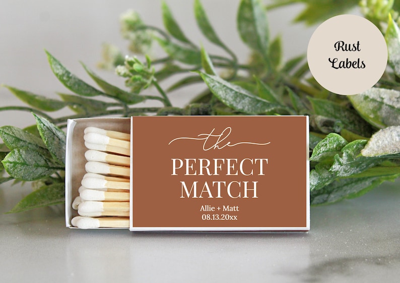 Peut inclure: Une bo&icirc;te d'allumettes rectangulaire avec une &eacute;tiquette couleur rouille portant le texte blanc "the PERFECT MATCH", les pr&eacute;noms "Allie + Matt" et la date "08.13.20xx". La bo&icirc;te est entrouverte, r&eacute;v&eacute;lant des allumettes en bois &agrave; bouts blancs.