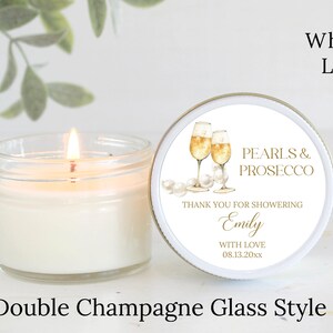 May include: A white candle jar with a white lid and a label that says "Pearls & Prosecco". The label also includes the text "Thank you for showering Emily with love 08.13.20xx". The label features a watercolor illustration of two champagne glasses.