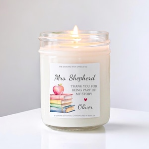 May include: A lit, white soy candle in a glass jar. The label reads "Mrs. Shepherd, THANK YOU FOR BEING PART OF MY STORY, Oliver" with an apple and books illustration. The candle is hand-poured in Bixby, OK.