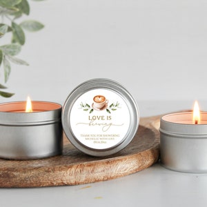 May include: Three silver candle tins with a white label on one tin. The label has a watercolor illustration of a coffee cup with a heart design and the text "Love is brewing". The text below the illustration says "Thank you for showering Michelle with love on her wedding day."