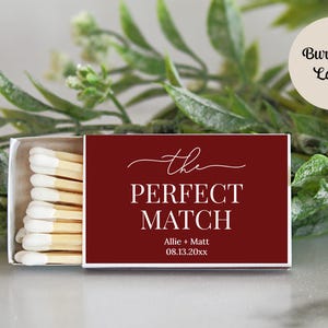Peut inclure: Une bo&icirc;te d'allumettes rectangulaire avec une couverture bordeaux fonc&eacute; portant le texte blanc 'the PERFECT MATCH' ainsi que les noms 'Allie + Matt' et la date '08.13.20xx'. La bo&icirc;te est entrouverte, r&eacute;v&eacute;lant des allumettes en bois &agrave; bouts blancs.