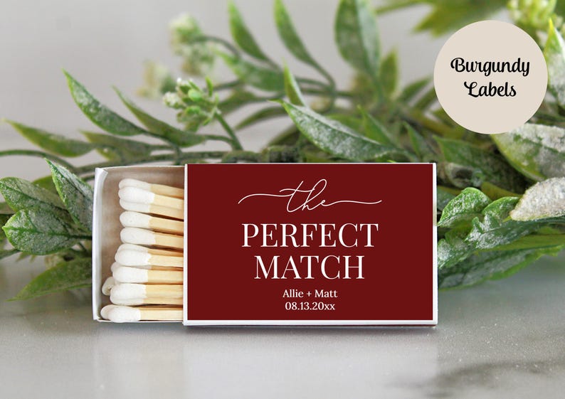 Peut inclure: Une bo&icirc;te d'allumettes rectangulaire avec une couverture bordeaux fonc&eacute; portant le texte blanc 'the PERFECT MATCH' ainsi que les noms 'Allie + Matt' et la date '08.13.20xx'. La bo&icirc;te est entrouverte, r&eacute;v&eacute;lant des allumettes en bois &agrave; bouts blancs.