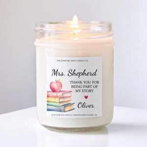 May include: A lit, white soy candle in a glass jar. The label reads "Mrs. Shepherd" with an apple and books illustration, and the text "Thank you for being part of my story." The candle is 8 oz and hand-poured in Bixby, OK.