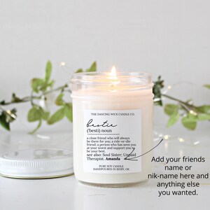 May include: A white candle in a glass jar with a white lid. The label on the jar reads "THE DANCING WICK CANDLE CO. bestie ('besti) noun a close friend who will always be there for you; a ride-or-die friend; a person who has seen you at your worst and support you to be your best. see also: Soul Sister; Unpaid Therapist. Amanda PURE SOY CANDLE HANDPOURED IN BIXBY, OK"