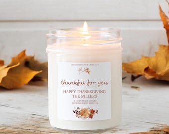 May include: A white soy candle in a clear glass jar with a label that reads "The Dancing Wick Candle Co. thankful for you Happy Thanksgiving The Millers 8 oz pure soy candle handpoured in Bixby, OK".