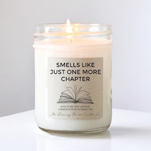 May include: A clear glass jar candle with a brown label that reads "Smells Like Just One More Chapter". The label also features a drawing of an open book and the text "8 oz Pure Soy Candle Handpoured in Bixby, OK The Dancing Wick Candle Co."