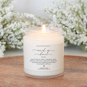 May include: A white candle in a glass jar with a label that reads "maid of honor noun best friend or sister, therapist, party planner, train fixer, bathroom assistant, someone the wedding would feel incomplete without" and "PURE SOY CANDLE HANDPOURED IN BIXBY, OK."