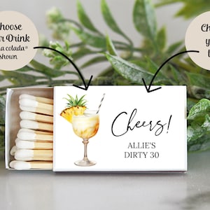 Puede incluir: Una caja blanca de cerillas con una ilustraci&oacute;n de un c&oacute;ctel de pi&ntilde;a y el texto "Cheers! Allie's Dirty 30".