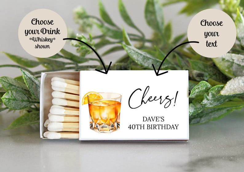 Puede incluir: Una caja de cerillas blanca con un dise&ntilde;o de un vaso de whisky con una rodaja de lim&oacute;n. El texto "Cheers! Dave's 40th Birthday" est&aacute; impreso en la caja de cerillas.