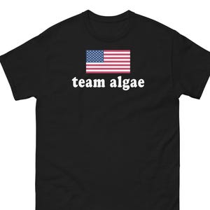 May include: A black short-sleeve t-shirt featuring a graphic of the United States flag centered above the white lowercase text that reads team algae. The shirt has a crew neckline and a standard fit, constructed from a solid black fabric.