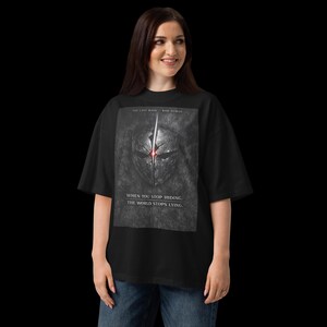 May include: Black t-shirt with a graphic of a futuristic mask with a red glowing centre. The text on the shirt reads "THE LAST MASK - RAW HUMAN" and "WHEN YOU STOP HIDING, THE WORLD STOPS LYING."
