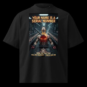May include: Black t-shirt with a graphic design. The design features a person with a fiery chest, chained, and the text "YOUR NAME IS A SERIAL NUMBER." Additional text includes "FROM THE FIRST CRY YOU ARE PROPERTY - THIS IS NOT ME."