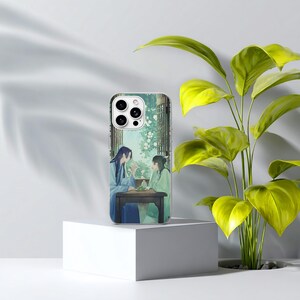 May include: A clear smartphone case featuring an illustration of two figures in traditional blue and green robes sitting at a dark wooden table. The scene is set against a backdrop of a window with white flowers and green foliage visible outside.
