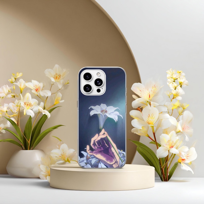 May include: A smartphone case featuring a graphic illustration of a hand holding a single white lily against a dark blue background. The case has a cutout for a triple-lens camera system and is displayed on a cylindrical stand.