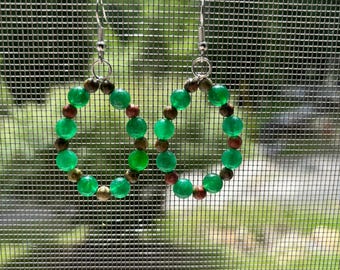 May include: A pair of hoop earrings featuring a circular arrangement of alternating bright green translucent beads and smaller, speckled brown and tan earthy beads, suspended from silver-toned metal fishhook ear wires for pierced ears.