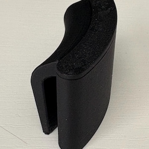 Op de afbeelding: Een zwart, U-vormig object met een getextureerd bovenoppervlak. Het object heeft een gebogen ontwerp en lijkt gemaakt te zijn van een mat materiaal. Het object staat rechtop tegen een witte achtergrond.