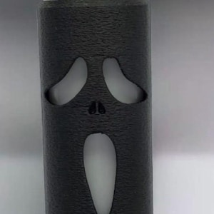 Puede incluir: Un encendedor negro con una superficie texturizada, con un dise&ntilde;o recortado de la m&aacute;scara de Ghostface de la franquicia Scream. El encendedor tiene un bot&oacute;n de encendido rojo y una parte superior de metal plateado.
