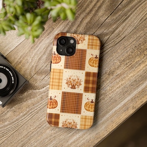 May include: A smartphone case featuring a patchwork design of alternating squares in shades of orange, brown, and cream. The pattern includes illustrations of pumpkins, plaid textures, and intricate floral motifs arranged in a grid layout.