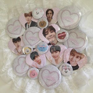 May include: A collection of circular and heart-shaped pin-back buttons featuring photographs of young people and cartoon characters. Several buttons display a white heart outline made of pearls with the text Bangtan forever.