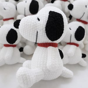 May include: Handmade white crochet dog plushies with black ear patches and a red collar. The dog's face has a smiling expression. Several of these plush toys are visible in the image, suggesting a collection or a batch of similar items.