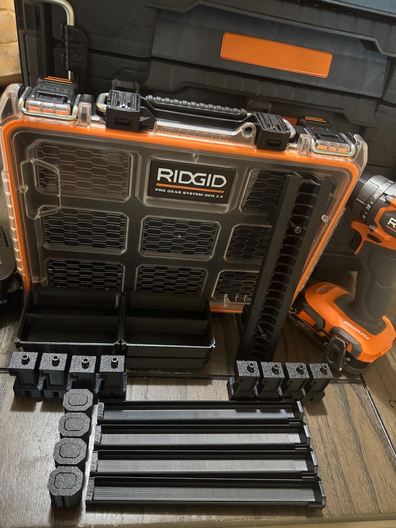 May include: An open black and orange RIDGID Pro Gear System Gen 2.0 tool case with various black tool organizers and an orange and black drill. The case is clear with a black grid design and the RIDGID logo.