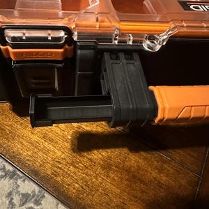 May include: Close-up of a black and orange RIDGID tool organizer. The organizer has a clear lid, orange accents, and a pull-out drawer. The RIDGID logo is visible on the front. The organizer is on a wooden surface.