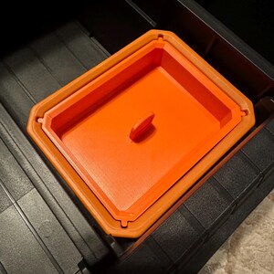 May include: An orange rectangular container with a handle, nested inside a larger orange container. The containers are inside a black storage bin. The containers have a textured surface.