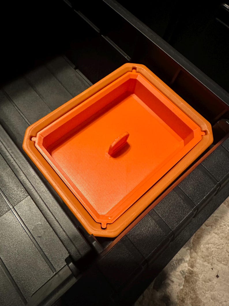 May include: An orange rectangular container with a handle, nested inside a larger orange container. The containers are inside a black storage bin. The containers have a textured surface.
