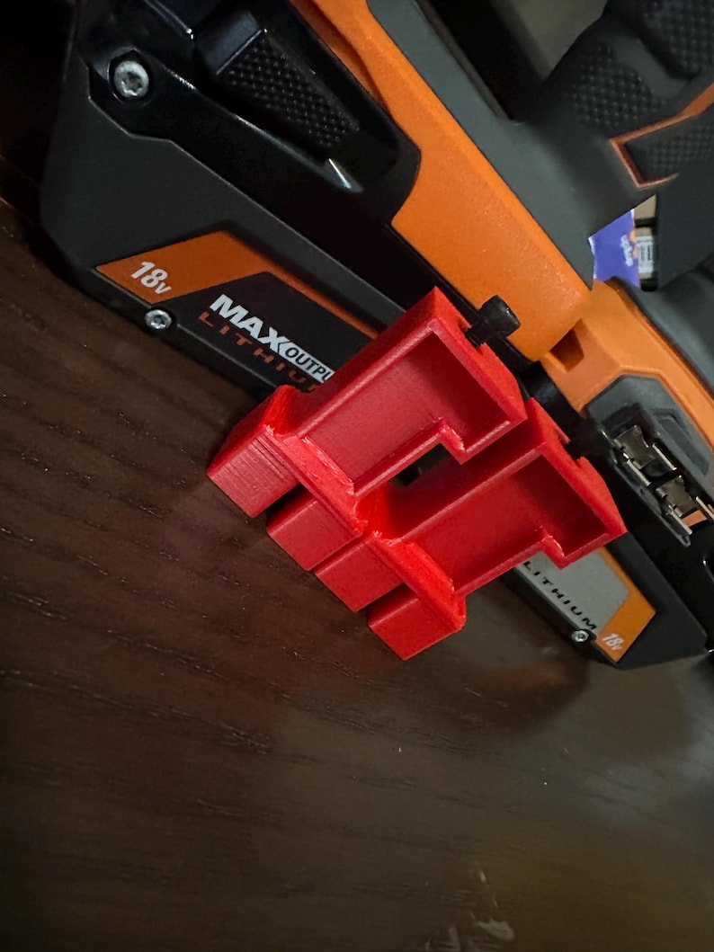 May include: A bright red 3D-printed tool attachment is positioned next to a black and orange power tool. The power tool has the text "MAX OUTPUT" and "18v" printed on it. The attachment has a unique, geometric design.