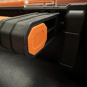 Puede incluir: Primer plano de una caja de herramientas negra y naranja. La caja de herramientas presenta un asa negra con un acento naranja. La tapa es transparente y el cuerpo es negro. La caja de herramientas est&aacute; dise&ntilde;ada para guardar herramientas y otros art&iacute;culos.