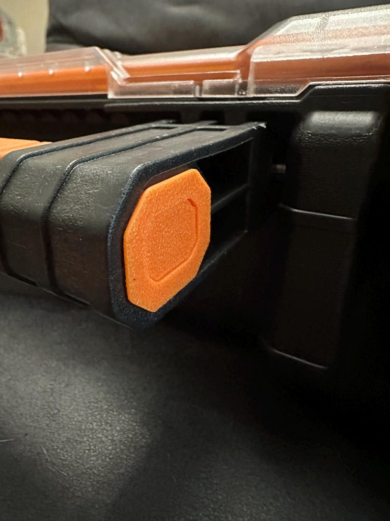 Puede incluir: Primer plano de una caja de herramientas negra y naranja. La caja de herramientas presenta un asa negra con un acento naranja. La tapa es transparente y el cuerpo es negro. La caja de herramientas est&aacute; dise&ntilde;ada para guardar herramientas y otros art&iacute;culos.