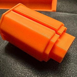 May include: Bright orange, 3D-printed object with a stepped, rectangular design. The object has a textured surface and appears to be a component or part of a larger structure. The color is consistent throughout the piece.