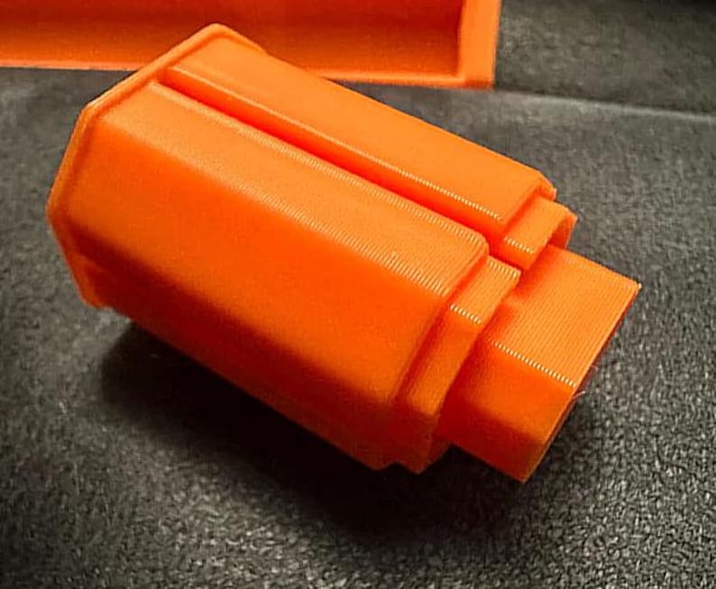 May include: Bright orange, 3D-printed object with a stepped, rectangular design. The object has a textured surface and appears to be a component or part of a larger structure. The color is consistent throughout the piece.