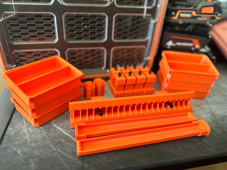 May include: An assortment of bright orange storage containers and organizers. The image shows several rectangular bins, cylindrical holders, and a rack-like organizer, all in a vibrant orange color. The items appear to be made of plastic and are designed for tool storage.