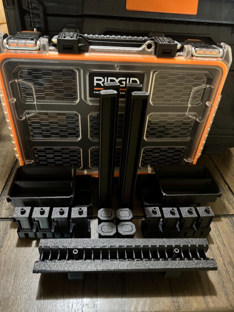 May include: A black and orange Ridgid Pro System tool box with various black storage components. The clear lid allows visibility of the contents. The tool box is open, displaying several black storage containers, dividers, and mounting pieces.