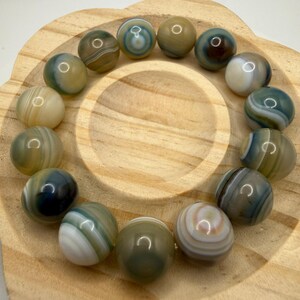 May include: A bracelet composed of smooth, spherical beads in shades of blue, green, brown, and white. Each bead features distinct, concentric banded patterns. The beads are arranged in a circular formation, showcasing a polished, glossy finish.