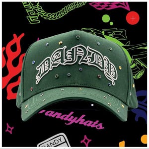 Può includere: Un cappellino da baseball verde bosco con la scritta DANDY in rilievo bianco sul davanti. Il cappellino è decorato con piccoli strass circolari colorati e minuscole borchie dorate a forma di piramide sparse sulla corona e sulla visiera.