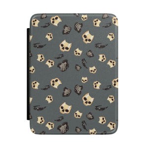 May include: A gray e-reader cover with a repeating pattern of tan skulls, rib cages, and sunglasses. The cover has a black elastic strap on the left side. The design is a spooky, Halloween-themed pattern.