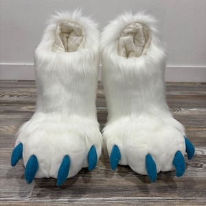 May include: A pair of white furry boots with large, padded feet and blue claws. The boots have a tall, open top with a quilted lining. The faux fur is long and fluffy, giving the boots a playful, animal-like appearance. These boots are likely part of a costume.