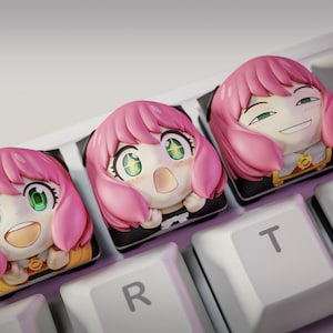 May include: Three custom keyboard keycaps featuring a pink-haired anime character with green eyes. The keycaps are on a white keyboard, with the character's face in different expressions. The keycaps are a unique accessory for keyboard enthusiasts.
