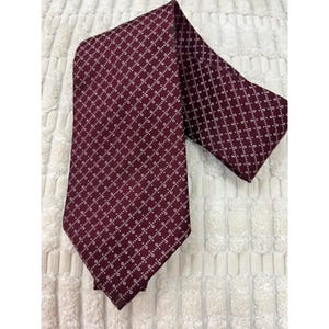 May include: A burgundy tie with a repeating white pattern of small, connected shapes. The tie is folded over, showing the front and back of the fabric. The fabric has a slight sheen.