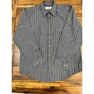 May include: Gray long-sleeve shirt with vertical white stripes. The shirt has a button-down front, a chest pocket, and buttoned cuffs. The collar has a small tag with text. The buttons are pink.