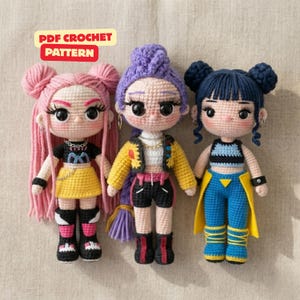 Op de afbeelding: Drie handgemaakte gehaakte poppen met garen haar en gedetailleerde outfits. De linkerpop heeft roze haar, de middelste pop paars haar en de rechterpop donkerblauw haar. De tekst bovenaan luidt PDF CROCHET PATTERN.