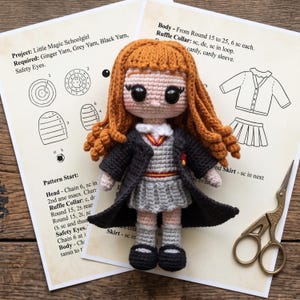 May include: A crocheted doll with ginger yarn hair, large black safety eyes, and a light skin tone. The doll wears a grey sweater vest, a pleated grey skirt, a white collared shirt, and a black robe. Beside the doll are printed pattern instructions.