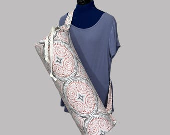May include: A yoga mat bag with a repeating pattern of red, gray, and white circular designs. The bag has a shoulder strap and a drawstring closure. The bag is displayed on a mannequin.